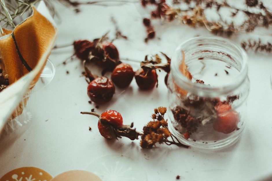 Aesthetic arrangement of dried rosehips and herbs in an open jar on a soft-toned surface.