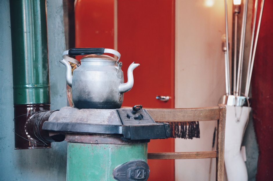 A vintage kettle rests on a rustic wood stove in an eclectic interior setting.